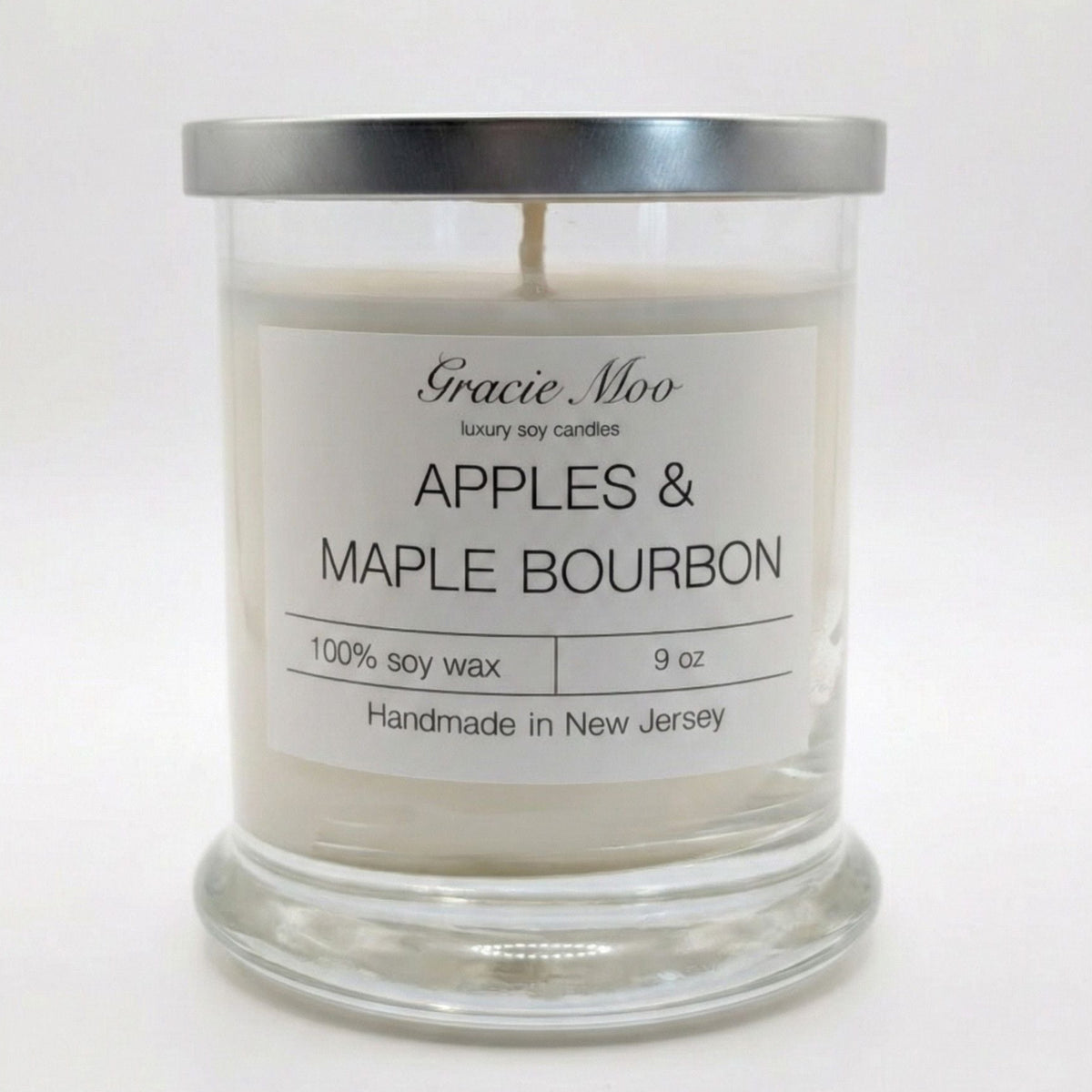 Gracie Moo Candles Apples & Maple Bourbon scented candle in a glass jar with a lit wick and warm glow.