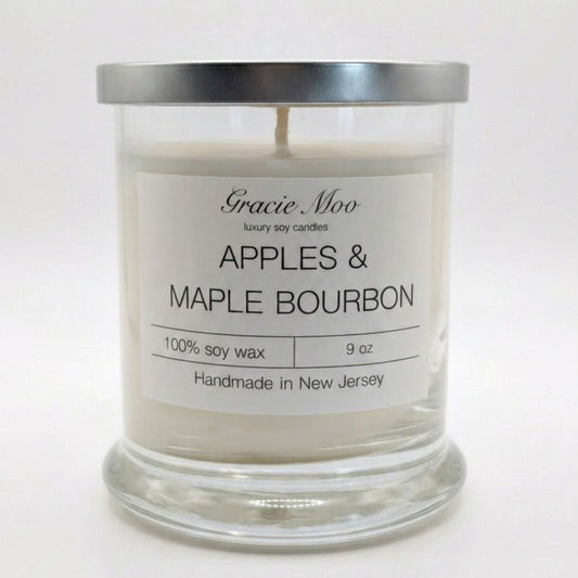 Gracie Moo Candles Apples & Maple Bourbon scented candle in a glass jar with a lit wick and warm glow.