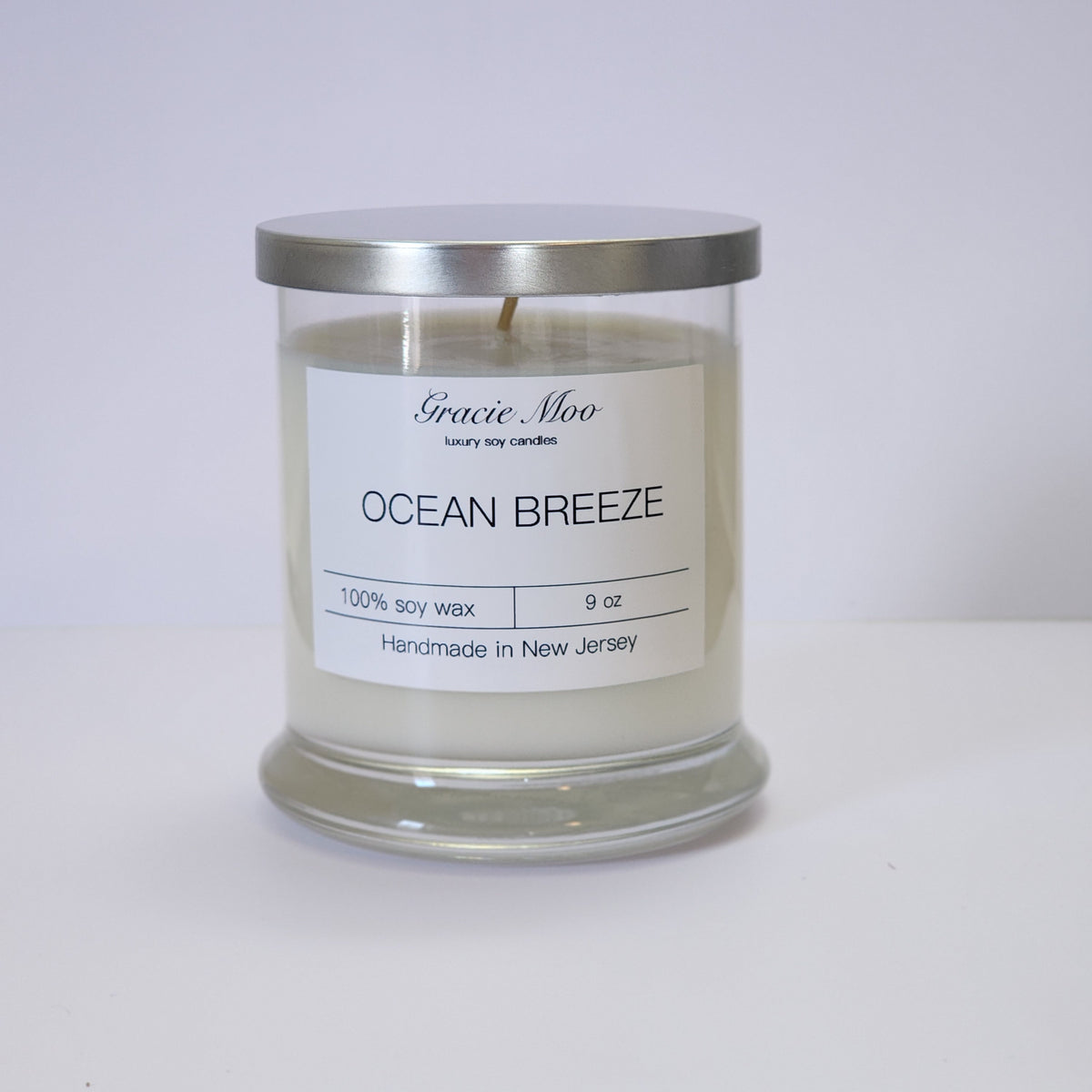 Ocean Breeze Status Candle by Gracie Moo Candles, showing a lit candle in a glass jar with ocean-inspired label and soft glow.
