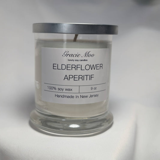 Elderberry Aperitif scented candle by Gracie Moo Candles, featuring a sleek glass jar with a lit wick and purple elderberry design.