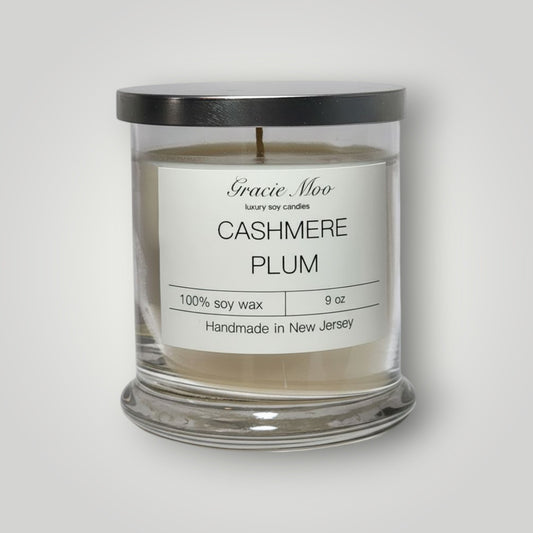 Gracie Moo Cashmere Plum Status Candle in a sleek glass container with a warm, inviting glow.