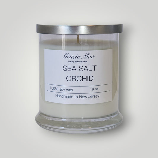 Sea Salt & Orchid Status Candle by Gracie Moo Candles featuring a sleek candle holder with a lit, aromatic candle in a serene setting.